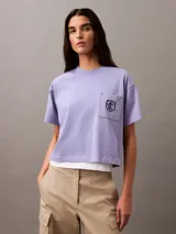 Remera lila de corte cropped y boxy, con cuello redondo y bolsillo en el pecho con escudo bordado en negro.