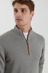 Sweater de punto gris con medio cierre frontal, cuello alto y coderas en tono marrón. Presenta un diseño clásico con puños y ruedo acanalados.