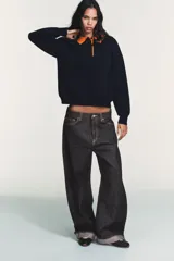 Jersey de punto de manga larga con cuello tipo polo en color naranja a contraste. Presenta cierre frontal con botones y diseño de corte holgado.