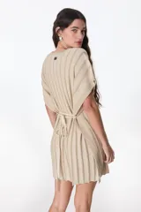 Vestido corto de tejido de punto color beige/crudo con hilos de lurex que le dan un brillo sutil. Diseño tipo poncho o caftán con mangas cortas y cuello redondo. Se ajusta a la cintura con un lazo fino del mismo material.