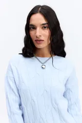 Buzo de punto color celeste con diseño de trenzas en relieve, cuello redondo y mangas largas con puños acanalados.