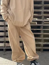 Pantalón deportivo de tiro alto en color beige, con diseño holgado, bolsillos laterales y puños elásticos en los tobillos. Presenta costuras verticales decorativas en el frente.