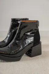 Botineta de cuero negro con textura de reptil, taco cuadrado y cierre trasero.