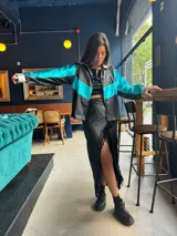 Campera corta de cuerina negra con mangas turquesas metalizadas y detalles plateados en cuello y puños.