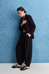 Pantalón negro de tiro alto y calce holgado, con pierna amplia, bolsillos laterales y puños ajustados con botones en los tobillos.