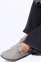 Zueco de gamuza color gris, con diseño de punta cerrada y tira ajustable con hebilla metálica sobre el empeine. Presenta una suela de corcho con base de goma negra.