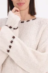 Sweater de punto grueso en color beige, con diseño de cuello redondo y detalle de pespuntes decorativos en color chocolate en el cuello, el ruedo y los puños.
