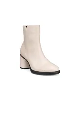 Botín de cuero liso color blanco hueso, de caña corta y punta redondeada. Posee un tacón ancho y bajo, y una suela negra gruesa.