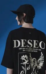 Remera de manga corta y cuello redondo con calce oversize. Presenta una estampa frontal en color crema con diseño artístico de un ángel y una rosa, acompañada de frases en español. Confeccionada en algodón premium.