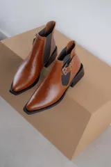 Botineta de cuero charol negro con acabado brillante, diseño de punta fina y taco cuadrado. Presenta un panel elástico lateral y una correa decorativa con hebilla metálica plateada.