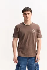 Remera de algodón marrón con efecto lavado, cuello redondo y manga corta. Cuenta con un pequeño estampado frontal de un sol estilizado y la inscripción "Mistral".