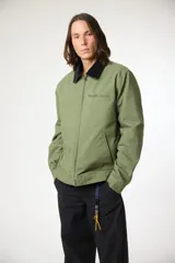 Chaqueta de lona color verde oliva con cuello de corderoy oscuro en contraste. Presenta cierre frontal completo, bolsillos laterales y un bolsillo horizontal con cierre en el pecho.