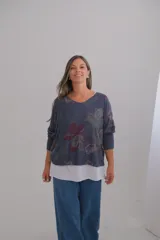 Sweter de corte amplio con diseño de doble capa, que presenta una capa superior estampada con motivos florales en tonos azules y una capa inferior blanca visible en el ruedo. Posee escote en V y mangas largas.