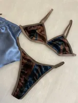 Conjunto de lencería compuesto por un bralette de corte triangular y una tanga regulable. Ambas piezas están confeccionadas en terciopelo con un estampado abstracto en tonos azul, marrón y negro, con terminaciones en ribete color marrón.