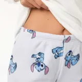 Conjunto de pijama de dos piezas confeccionado en tela polar suave. Incluye una remera de manga larga color blanco con estampa central de Stitch y un pantalón largo color gris claro con estampado integral de Stitch.