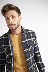 Sobrecamisa de viyela para hombre con estampado de cuadros en rojo y negro. Presenta cierre frontal con botones, bolsillos en el pecho con solapa y botón, y un interior capitoneado para mayor abrigo. Cuenta con un logo en grifa de cuero.