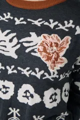 Buzo de tejido de punto en color beige con estampado de motivos florales y abstractos en tonos marrones. Presenta cuello redondo con borde en color azul vibrante, mangas largas y puños ajustados.