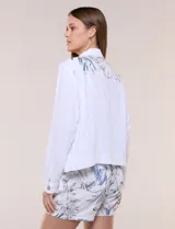 Campera liviana de lino color blanco, con estilo denim y silueta semi entallada. Presenta un canesú superior estampado con motivos florales en tonos azules y tostados, cuello camisero, abotonadura frontal con botones rústicos y bolsillos con solapa en el pecho.