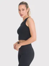 Top crop sin mangas de color negro, confeccionado en tejido acanalado con cuello redondo. Presenta un diseño ajustado al cuerpo con una pequeña abertura en la espalda y una cinta decorativa.