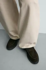 Mocasines de vestir color marrón oscuro, confeccionados en piel con acabado en gamuja serraje. Presentan detalle de antifaz en el empeine con costuras pespunteadas, punta redonda y suela track de goma robusta.