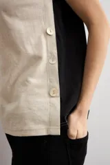 Remera sin mangas de diseño bicolor, con frente color beige y espalda negra, escote en V y detalle de botones laterales.