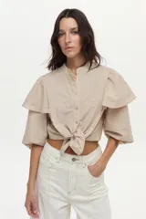Camisa de algodón a rayas color beige y blanco, con cuello mao, volados en los hombros, mangas abullonadas y nudo frontal en el dobladillo.