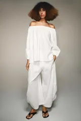 Blusa blanca de lino con escote recto y hombros descubiertos, manga abullonada tres cuartos terminada en elástico.