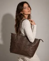 Cartera tipo tote bag de cuero vacuno color marrón oscuro, de diseño estructurado con asas largas para llevar al hombro y cierre superior. Presenta detalles de costuras decorativas y pespuntes en el frente.