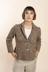 Chaqueta marrón de lana con cuello, solapa y bolsillos ojal. Forro solo en las mangas y terminaciones envivadas. Esquinas redondeadas y mangas con corte en puño que permiten transformarla en manga 3/4. Más larga en la espalda que en la delantera. Abrochadura con dos botones.