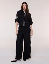 Conjunto de dos piezas negro compuesto por camisa de manga corta con cuello camisero y pantalón palazzo de tiro alto. Presenta detalles de bordados florales en contraste a lo largo de los laterales del pantalón y en las mangas.