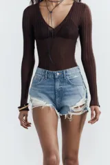 Short de jean negro desgastado, tiro alto, con roturas pronunciadas y terminación deshilachada en el bajo. Presenta cinco bolsillos y cierre frontal con botón metálico.