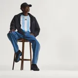 Pantalón de denim azul de corte holgado, tiro medio y diseño clásico con las tres tiras características de Adidas a lo largo de los laterales.