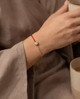 Pulsera de hilo rojo de seda combinada con cadena de acero con baño de oro, con un dije redondo central tipo punto de luz engastado con circorias.