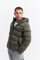 Campera puffer con capucha, color verde militar, con cierre frontal y bolsillos laterales con cierre. Diseño acolchado de volumen medio.