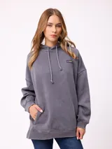 Canguro oversize de color gris con efecto lavado, capucha con cordones ajustables, bolsillo frontal tipo canguro y parche pequeño con logo de la marca en el pecho.