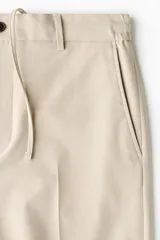 Pantalón de vestir color beige, de corte relajado, con bolsillos laterales y traseros, y raya marcada en las piernas.