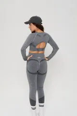 Conjunto deportivo de dos piezas compuesto por un top de manga larga con abertura en la espalda y calzas de tiro alto con diseño de contorno moldeador. Ambas prendas presentan un acabado jaspeado y detalles de tejido técnico con textura.