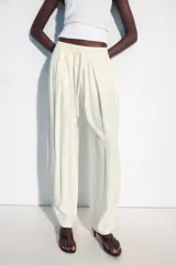 Pantalón fluido de tiro medio, color blanco, con cintura elástica ajustable con cordones, bolsillos laterales y bajo ajustable con trabilla y botón a presión.