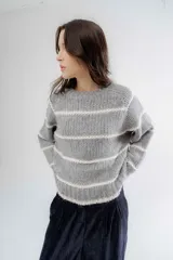 Buzo de tejido de punto grueso en color gris con rayas horizontales en color crema, de corte holgado, cuello redondo y mangas largas.