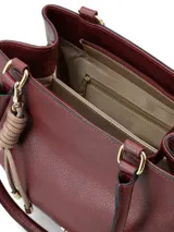 Cartera de hombro color bordó con textura granulada, diseño estructurado y herrajes dorados. Incluye un detalle decorativo de nudo en tono beige claro y logo metálico en la parte frontal.