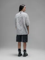 Camisa de manga corta color beige con cuello clásico y cierre de botones. Presenta un diseño de bordado calado con motivos florales y geométricos.