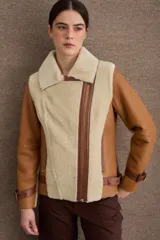 Chaqueta tipo gamulán de cuero color camel con interior y solapas de piel sintética en color beige. Presenta cierre frontal cruzado, correas ajustables con hebillas en los puños y en la cintura, y diseño de cuello solapa.