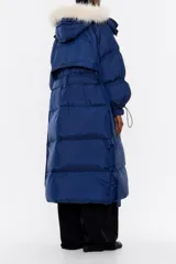 Plumífero largo azul con relleno de pluma y plumón, cuello alto, manga larga, cierre frontal con cremallera, botones de presión y cinturón. Tiene bolsillos laterales y capucha extraíble con pelo a contraste.