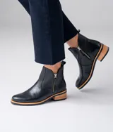 Botas cortas de cuero vacuno color marrón, con diseño de caña baja y cierre metálico en ambos laterales. Presentan un taco cuadrado de madera y suela de goma.