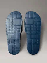 Chinelas de color azul con banda superior de material textil que presenta el logotipo de Calvin Klein bordado en blanco. La suela es ergonómica y antideslizante, con el nombre de la marca grabado en el lateral.