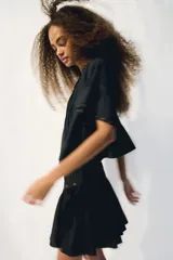 Pollera corta negra con cintura en V decorada con ojales metálicos. Presenta pliegues en la parte superior y un frunce que da volumen a la falda.