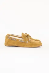 Mocasín de cuero gamuzado color pistacho, con detalle de cordones decorativos y argollas metálicas plateadas en los laterales. Presenta un lazo frontal y suela plana.