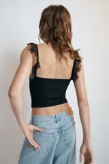 Top corsetero blanco con escote cuadrado y tirantes anchos con volados de encaje. Presenta costuras marcadas y cierre frontal con ganchos metálicos.