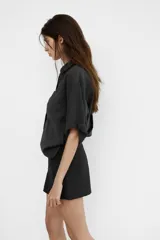 Camisa de corte fluido confeccionada en mezcla de modal, con cuello solapa, manga corta con dobladillo y bolsillo de plastrón en el delantero. Presenta cierre frontal con botones ocultos por tapeta y aberturas laterales en el bajo.