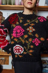 Sweater de lana tejido a mano color negro con bordado de flores rosas, naranjas y rojas. Tiene cuello redondo y mangas largas con puños ajustados.
